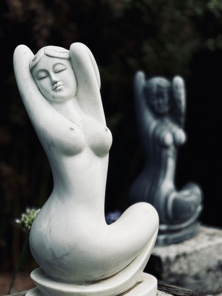 Pale and dark stone figures of women in a garden