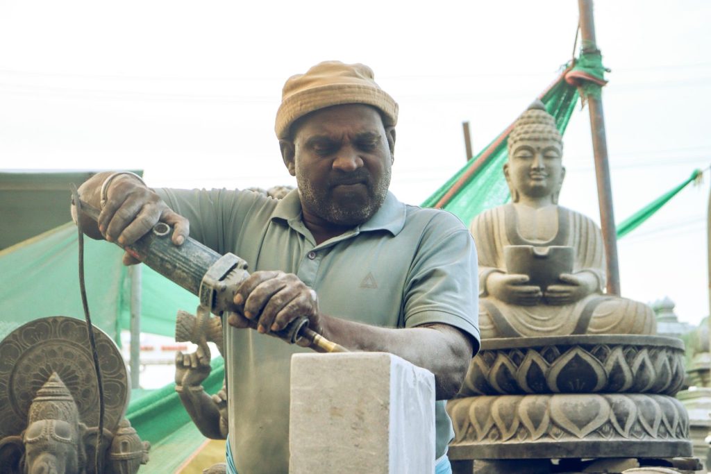 Artisan carving a stone statue in an outdoor workshop