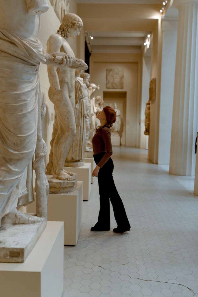 A visitor studying sculptures along a gallery corridor