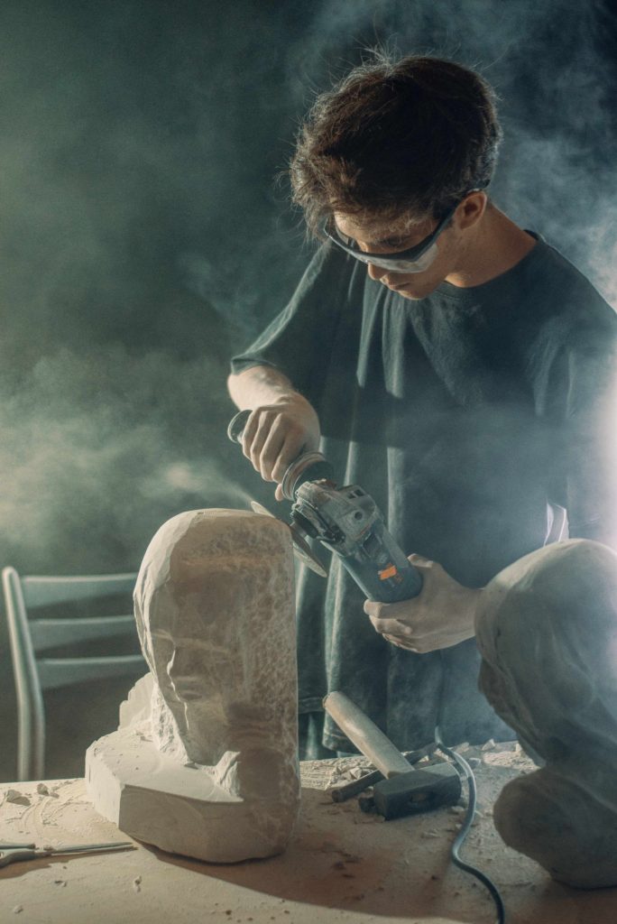 Sculptor carving stone amid a haze of stone dust