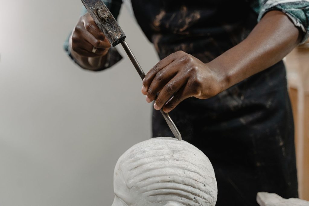 Hands guiding a chisel across a carved stone head
